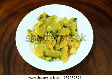 Stir-fried pumpkin with eggs in a white plate on the wooden background.Pumpkin and egg stir fry in thai style. Homemade Stir Fried Pumpkin and have a With beta carotene with good healty.