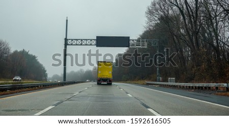 Blank electric digital road sign over a highway with a yellow truck directly underneath it
