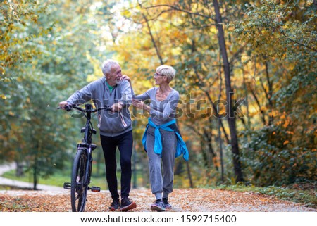 Mature couple woman and man with bicycle walking in the park and talk
