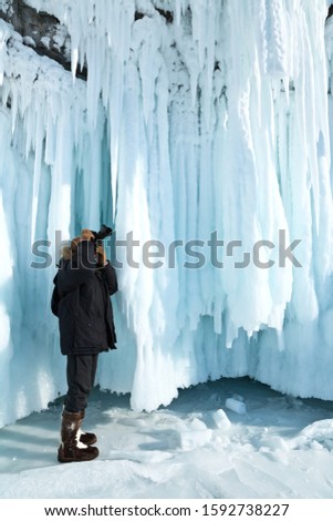 Winter Baikal Lake. A tourist photographs amazing ice crust with long icicles on the rocks of Olkhon Island on cold February day. Ice travel on frozen lake