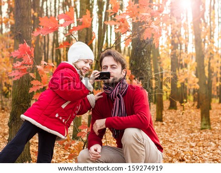 Girl child and father taking outdoor photo with mobile phone in an autumn park - enjoying modern technology