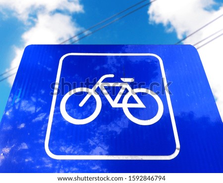 Square blue and white arrow road sign for pedestrian and bicycle areas, mounted on metal poles, intentionally blurred shot against blue sky background