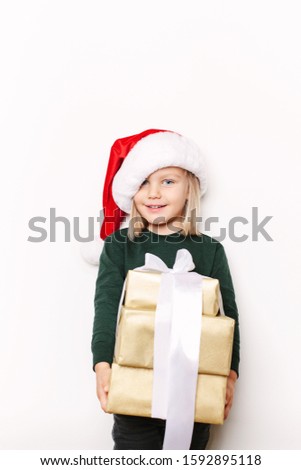 Funny smiling kid wearing santa hat and holding gift boxes. Blonde hair and blue eyes. Studio shot. White backgroud, not isolated.