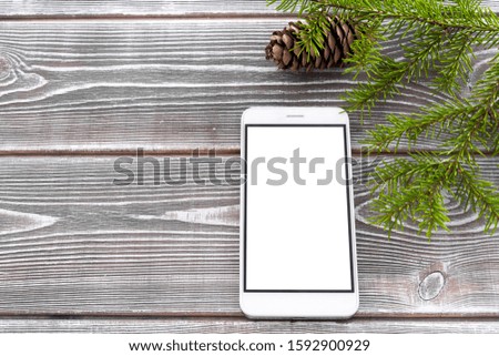 Branch of spruce with a cone, smartphone with a white screen on a wooden background