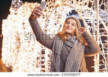 A beautiful girl doing selfie outdoors in front of Christmas holidays decorations.