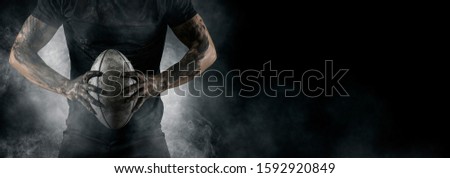 Rugby football player holds ball. Sports banner. Horizontal copy space background Royalty-Free Stock Photo #1592920849