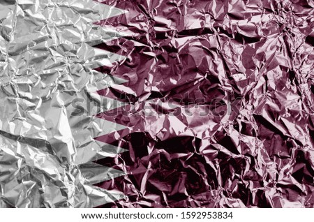 Qatar flag depicted in paint colors on shiny crumpled aluminium foil closeup. Textured banner on rough background