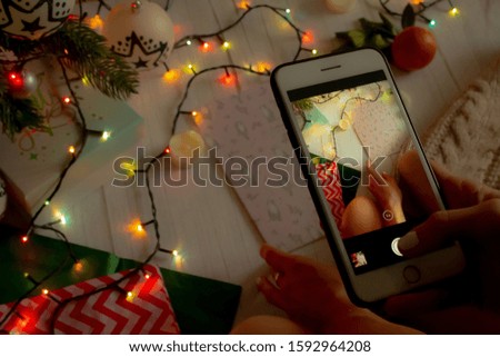 New Year concept, a girl takes a New Year's photo by the Christmas tree on the phone, a luminous garland, candles and gifts. Top view for new year or christmas banner. background