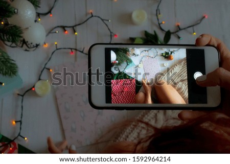 New Year concept, a girl takes a New Year's photo by the Christmas tree on the phone, a luminous garland, candles and gifts. Top view for new year or christmas banner. background