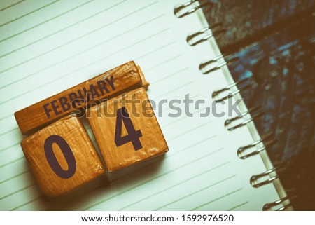 february 4th. Day 4 of month,Handmade wood cube with date month and day placed on a lined notebook on a blue background. artistic coloring.  winter month, day of the year concept