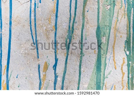 Multi-colored streaks of paint flow down an old white wall with cracks