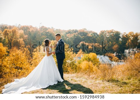 Beautiful newlyweds are standing on a hill on a background of autumn forest.