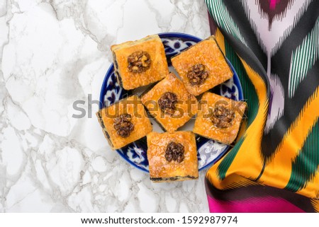 Traditional arabic dessert baklava with cashew, walnuts, raisins on plate with Uzbek national ornament on grey marble table. Homemade baklava with nuts and honey Top view Flat Lay