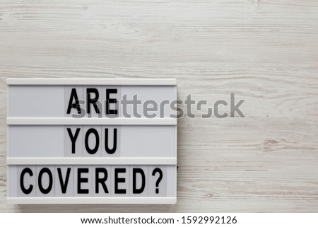 'Are you covered?' words on a modern board on a white wooden surface, top view. Overhead, from above, flat lay. Space for text.