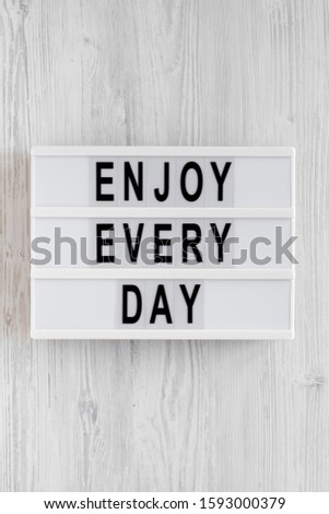 'Enjoy every day' words on a lightbox on a white wooden background, top view. Overhead, from above, flat lay. 