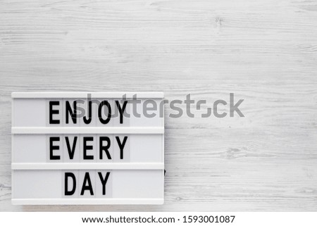 'Enjoy every day' words on a modern board on a white wooden background, top view. Overhead, from above, flat lay. Copy space.