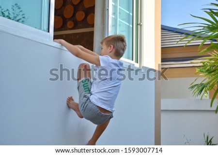 The boy climbs out the open window. The child climbs into the room through an open window. Boy teen climbs out the window home. Active children's leisure in the summer. funny kids games outdoor. 
