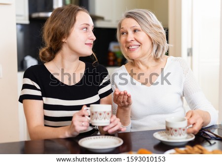 Smiling elderly and young women enjoying time at home, drinking tea together