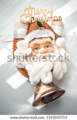 Sata Claus in glasses holds the text Merry Christmas in his hands, a large bell part of the toy