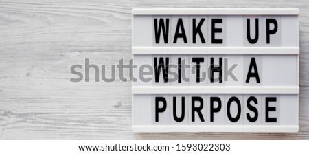 'Wake up with a purpose' words on a lightbox on a white wooden surface, top view. Overhead, from above, flat lay. Space for text.