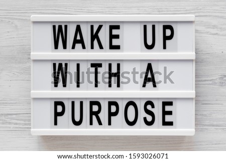 'Wake up with a purpose' words on a modern board on a white wooden background, top view. Overhead, from above, flat lay. Close-up.