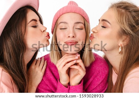 Portrait closeup of young happy women wearing pink clothes kissing girlfriend on her cheeks isolated over white background