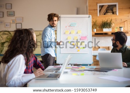 Startup leader drawing flowchart on board and discussing project with team. Business colleagues in casual working together in contemporary office space. Teamwork concept