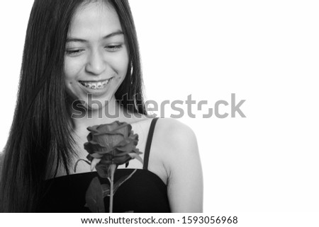 Young happy Asian teenage girl smiling while holding red rose