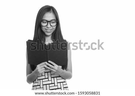 Young happy Asian teenage nerd girl smiling while reading book