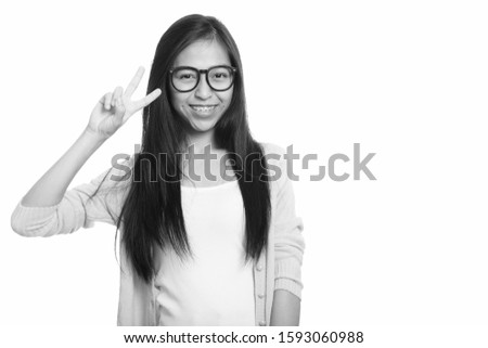 Studio shot of young happy Asian teenage girl smiling and giving peace sign