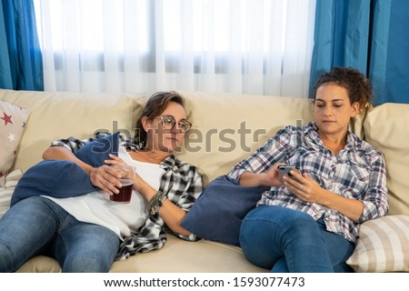 Stock photo of two girls lying on a sofa with their mobile phone and a glass of soda