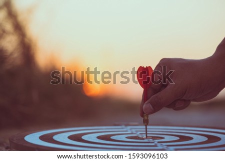 Close up hand hitting red arrow to target dartboard at sunset background. Business targeting and focus concept.