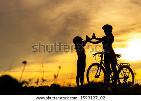 Silhouette biker lovely family raise give me five at sunset for relax and freedom. Mom and daughter bicycling at the beach. Lifestyle Concept.
