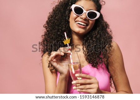 Image of laughing african american woman in sunglasses drinking champagne isolated over pink background