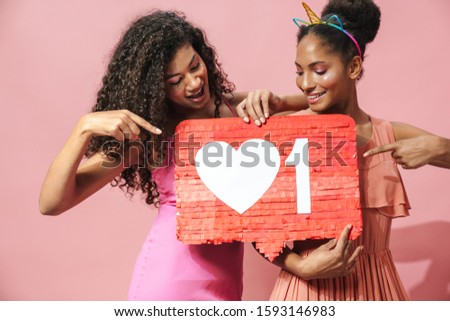 Image of laughing african american women holding placard and pointing fingers isolated over pink background