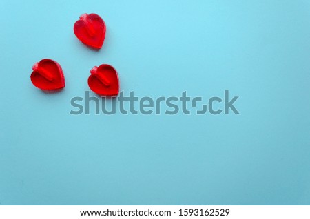 Valentine's flat lay with three small crushed red love hearts on colorful blue background, greeting card copy space top view. Valentine's day celebration