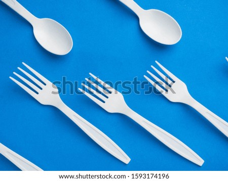 Plastic white disposable biodegradable fork and spoon on a trendy blue color background. Concept plastic dishes, fast food, plastic pollution. Top view, flat lay. Trend of 2020 color