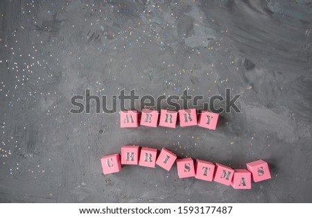 Merry Christmas greeting in 3D wooden pink cubes alphabet letters on concrete background with copy space.