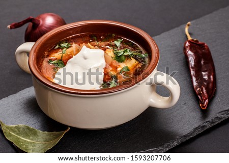 Ukrainian traditional borsch in porcelain bowl with sour cream, onion and chilli pepper on black stone board. Top view.