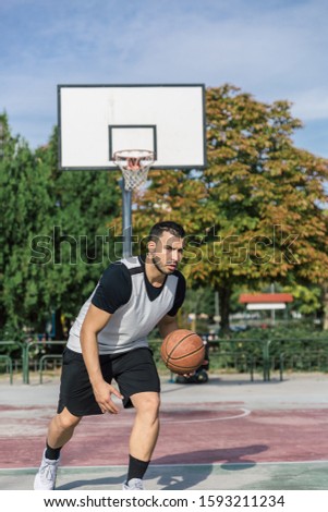 Urban athlete practices basketball on an outdoor court of a city playing with the ball with his left arm