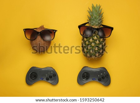 Gamer concept. Fun and humor. Pineapple and coconut in sunglasses and gamepad on yellow background. Top view