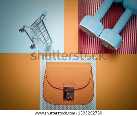 Buyer, shopaholic concept. Bag, mini shopping trolley, sport dumbbells on a creative background. Minimalism. Top view. Flat lay