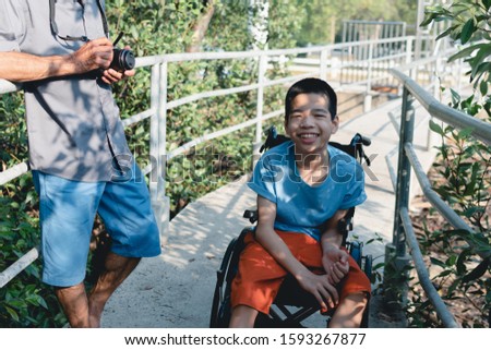 Asian special child on wheelchair is happily on mangrove forest background, Excited to travel on a holiday with his father, Life in the education age of disabled children, Happy disabled kid concept.