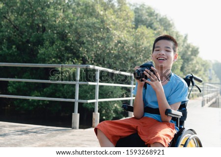 Asian special child on wheelchair is happily on mangrove forest background, Excited to travel on a holiday, He has camera, Life in the education age of disabled children, Happy disabled kid concept.