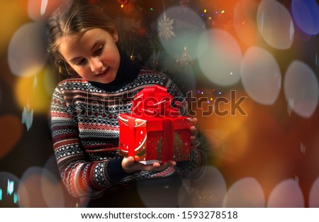 Cheerful girl with a gift in her hands on a dark background with a beautiful festive bokeh. Merry Christmas