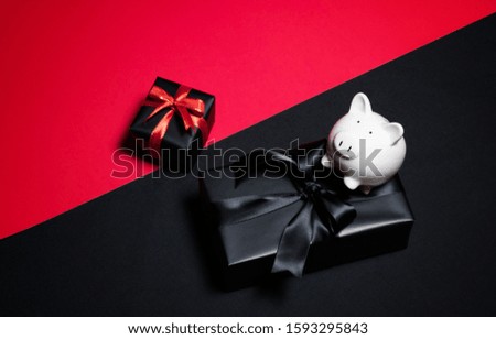 Top view of gift box with red, black ribbons and piggy bank isolated on red and black background. Shopping concept boxing day and black Friday sale composition.