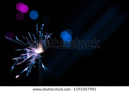 Burning sparkler in blue and white light on a black background. Closeup photo of Christmas and new year sparkler. Can be used like a wallpaper or postcard.
