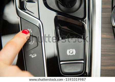 the finger of a female hand push the parking assistant button, the equipment of a modern car. close-up, soft focus, blur background