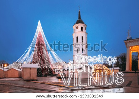 Vilnius, Lithuania. Christmas Tree, Sign "Greetings From Vilnius" Near Bell Tower Of Vilnius Cathedral At Cathedral Square In Evening New Year Christmas Xmas Illuminations. Unesco World Heritage Site.