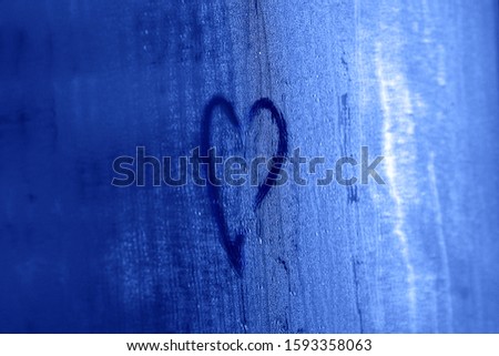 Heart drawn on steamed wet misted glass mirror surface toned blue color of 2020